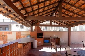An outdoor patio with a brick wall, a grill, and a table with chairs. - Residencial c/Serviços frente mar. (Rio de Janeiro)