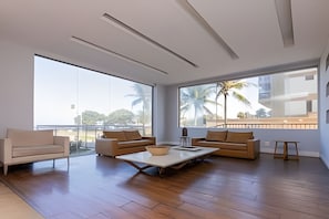 A spacious living area with a large window, a sofa, a coffee table, and a small table with a bowl. - Residencial c/Serviços frente mar. (Rio de Janeiro)