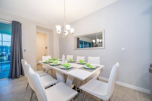 A dining area with a table set for six, white chairs, a chandelier, and a large mirror on the wall. - Solara Resort 5BR Home with Private Pool (Kissimmee)