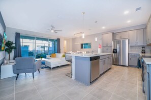 A modern kitchen with a central island, stainless steel appliances, and a dining area with a white sofa. - Solara Resort 5BR Home with Private Pool (Kissimmee)