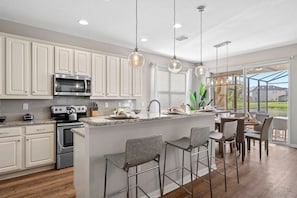 A modern kitchen with white cabinetry, stainless steel appliances, and a bar area with metal chairs. - 8BR Near Disney Private Pool, spa & Lake View (Kissimmee)