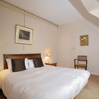 Un dormitorio con una cama grande, una mesita de noche, una silla y dos cuadros en la pared.