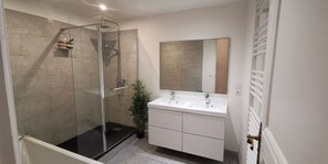 Ein modernes Badezimmer mit einer gläsernen Duschkabine, einem weißen Waschtisch mit zwei Becken und einem großen Spiegel darüber.
