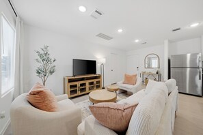 Una sala de estar moderna con un televisor de pantalla plana, un sofá, una mesa de centro y un comedor con una encimera de cocina.