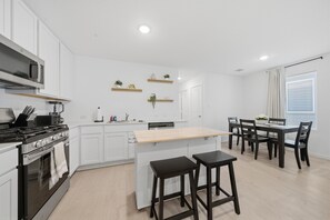 Una cocina moderna con armarios blancos, una isla central y un comedor con mesa y sillas.