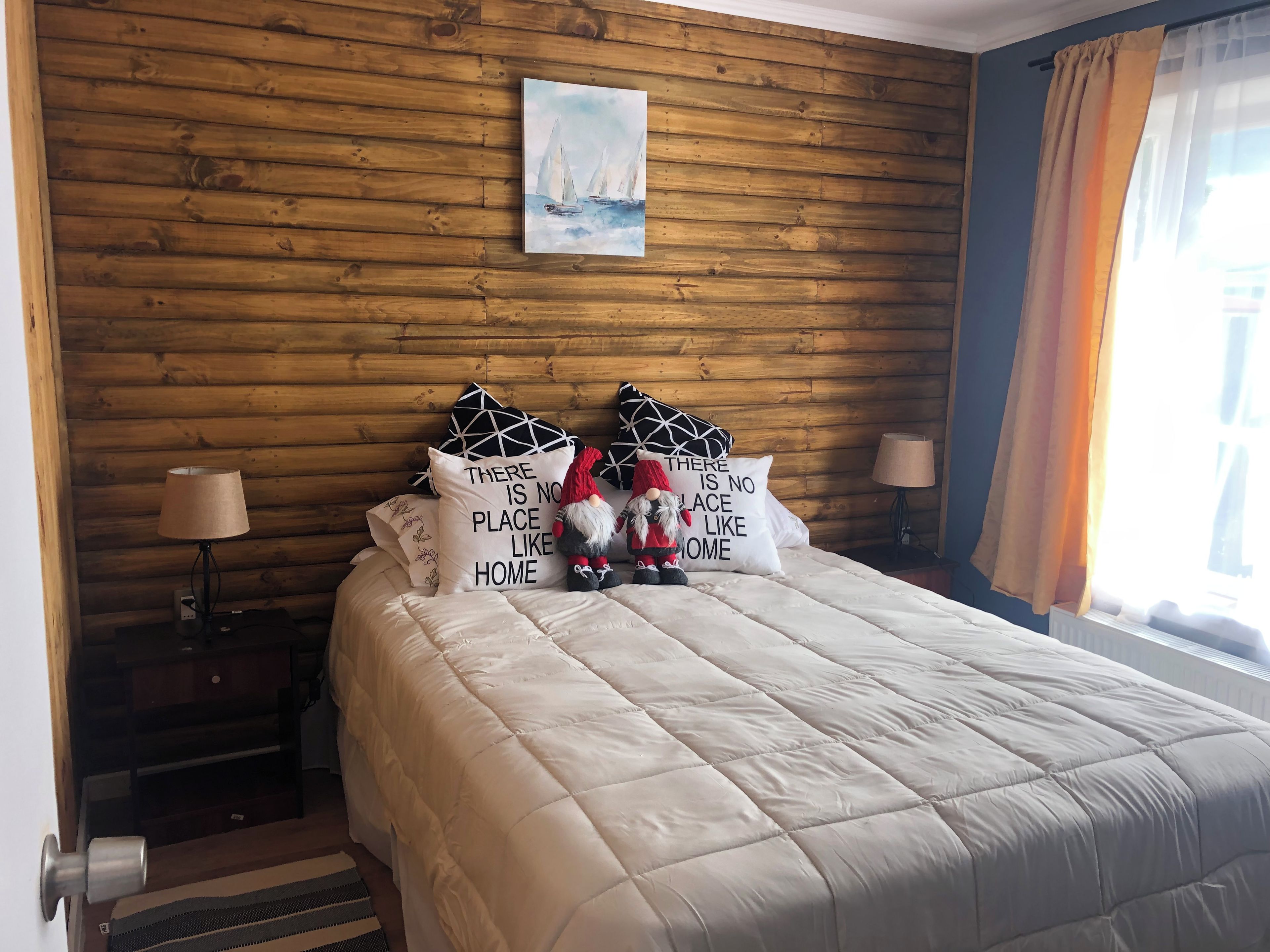 Un dormitorio con pared de madera, un cuadro y almohadas decorativas.