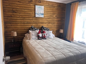 A bedroom with a wooden wall, a painting, and decorative pillows. - Comfortable, centrally located cabin in Puerto Natales (Puerto Natales)