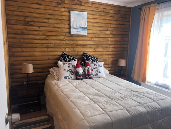 A bedroom with a wooden wall, a painting, and decorative pillows. - Comfortable, centrally located cabin in Puerto Natales (Puerto Natales)