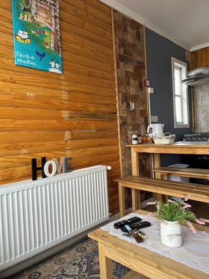 Ein Zimmer mit Holzwandverkleidung, einem weißen Heizkörper, einer Küchenzeile mit Herd und einem Tisch mit Vase und Schlüsseln.