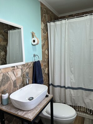 A bathroom with a stone wall, a white sink, a mirror, a towel, and a shower curtain. - Comfortable, centrally located cabin in Puerto Natales (Puerto Natales)