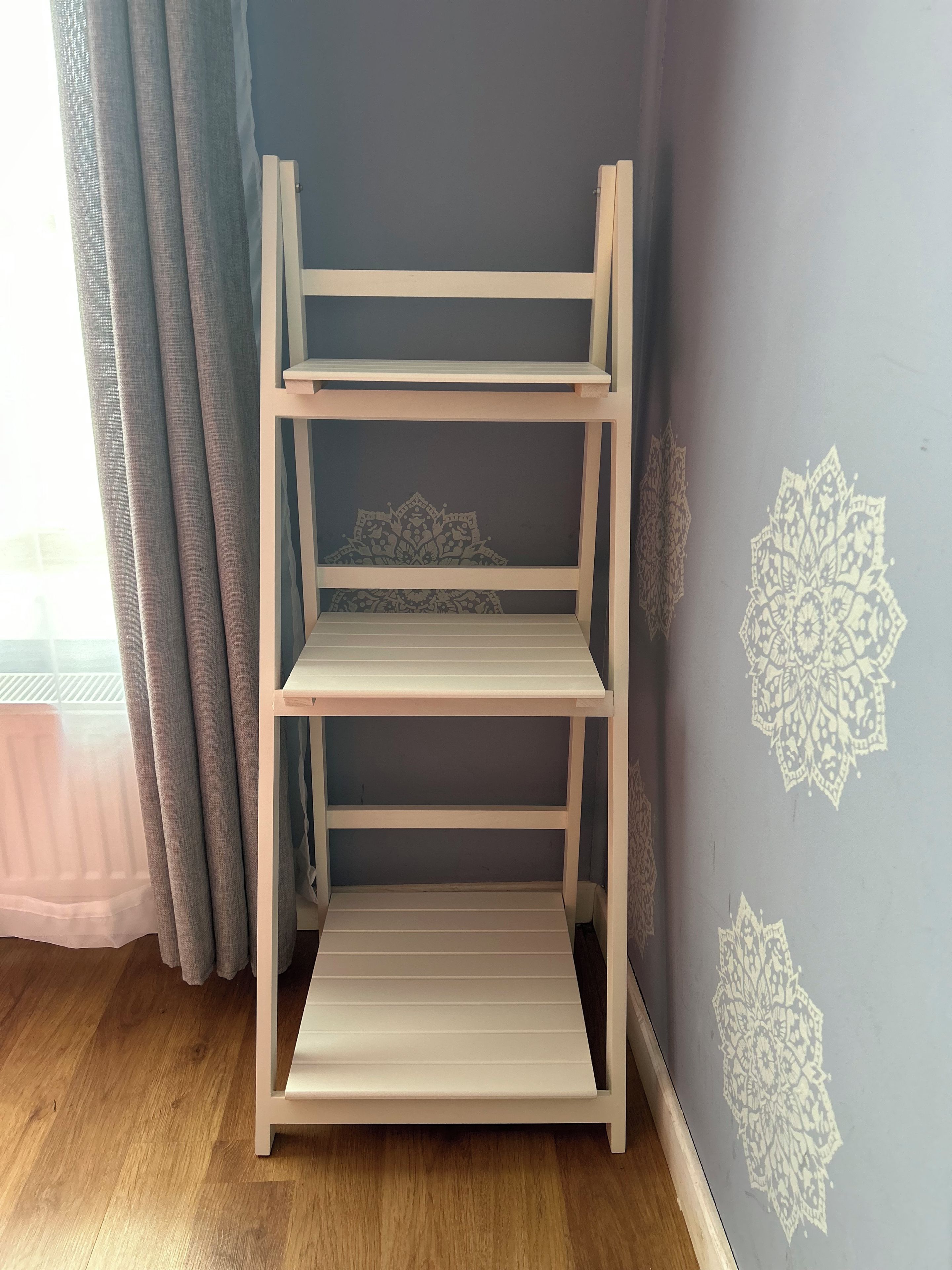 A white shelf unit with three shelves against a wall with decorative patterns.