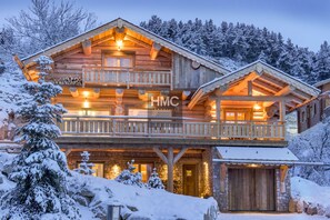 A two-story log cabin with a balcony, stone foundation, and a wooden garage. - Nanook, luxe montagnard, sauna et jacuzzi (Bolquère)