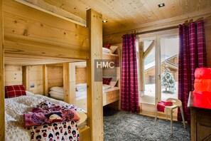 Eine Holzhütte mit Etagenbetten, einer kleinen Sitzecke und Blick auf eine verschneite Landschaft.