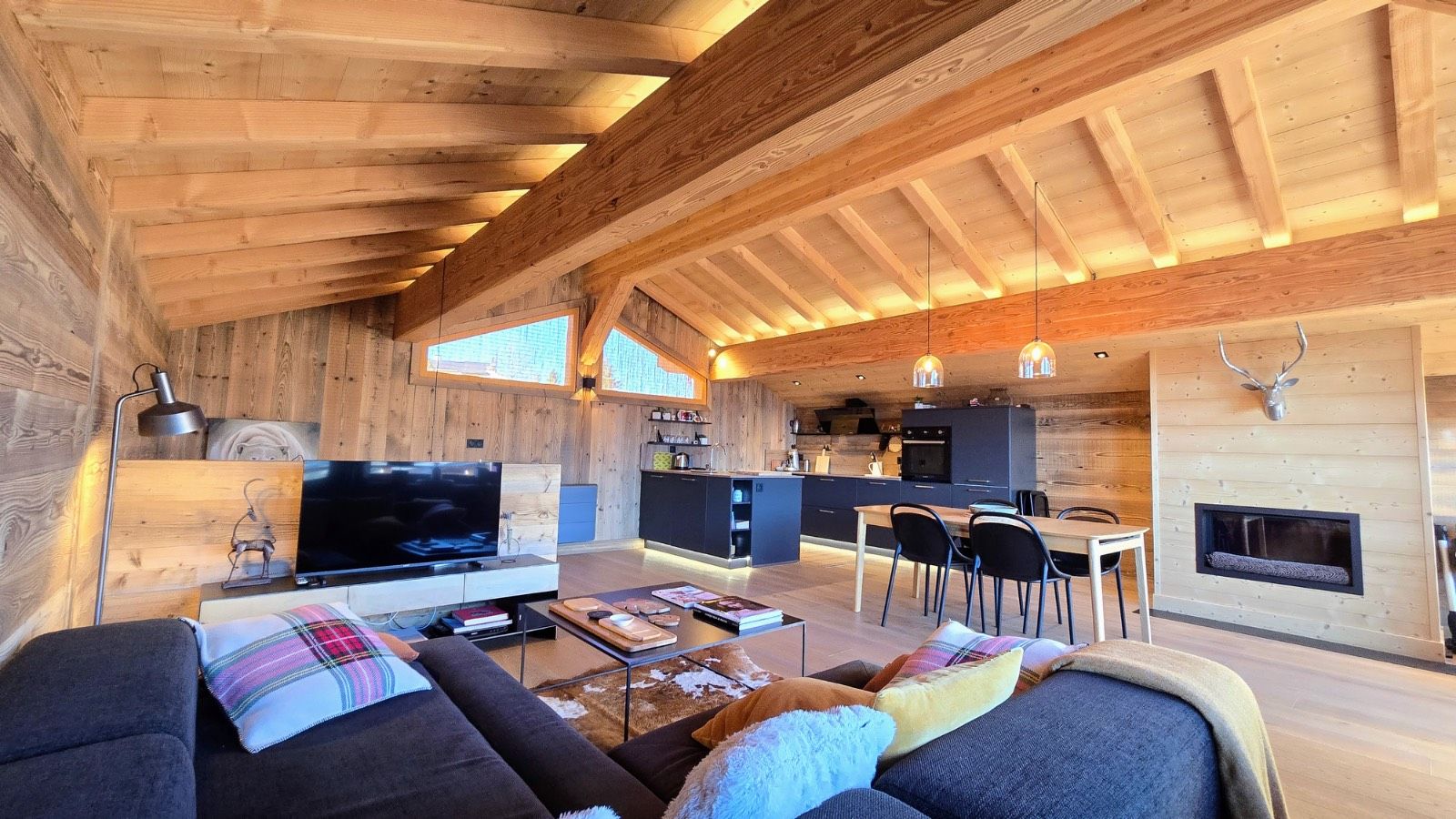 A modern log cabin interior with a living room, dining area, kitchen, and fireplace.