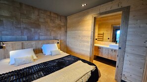 A bedroom with a wooden headboard, a bed with white linens, a black and beige blanket, and a wooden door leading to a bathroom. - Chalet 4 Saisons, ski aux pieds (Les Angles)