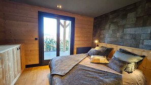 A bedroom with a large bed, wooden walls, a stone accent wall, and a sliding glass door leading to an outdoor area. - Chalet 4 Saisons, ski aux pieds (Les Angles)