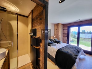 Ein modernes Schlafzimmer mit einem großen Bett, einer Duschkabine aus Glas und Seeblick.