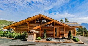 A wooden cabin with a sign reading 'HMC' and a covered porch. - Chalet "Cosy Nest", superbe vue, calme (Les Angles)