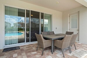 A patio with a table and chairs, a sliding glass door, and a pool in the background. - 5BR Near Disney Pool, spa & Game Room (Kissimmee)