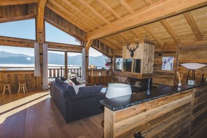 A wooden cabin interior with a sofa, a dining area, and a view of mountains. - Chalet "Nest Lodges" (Les Angles)