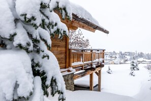 Eine Holzhütte mit Balkon, umgeben von schneebedeckten Bäumen und einer verschneiten Landschaft.