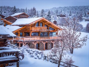 A wooden chalet with a balcony, surrounded by snow-covered trees and a mountainous backdrop. - Le Levant, Écrin de lumière, vue et Jacuzzi (Bolquère)