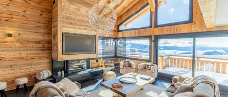 A cozy living room with a fireplace, comfortable seating, and a large window offering a mountain view.