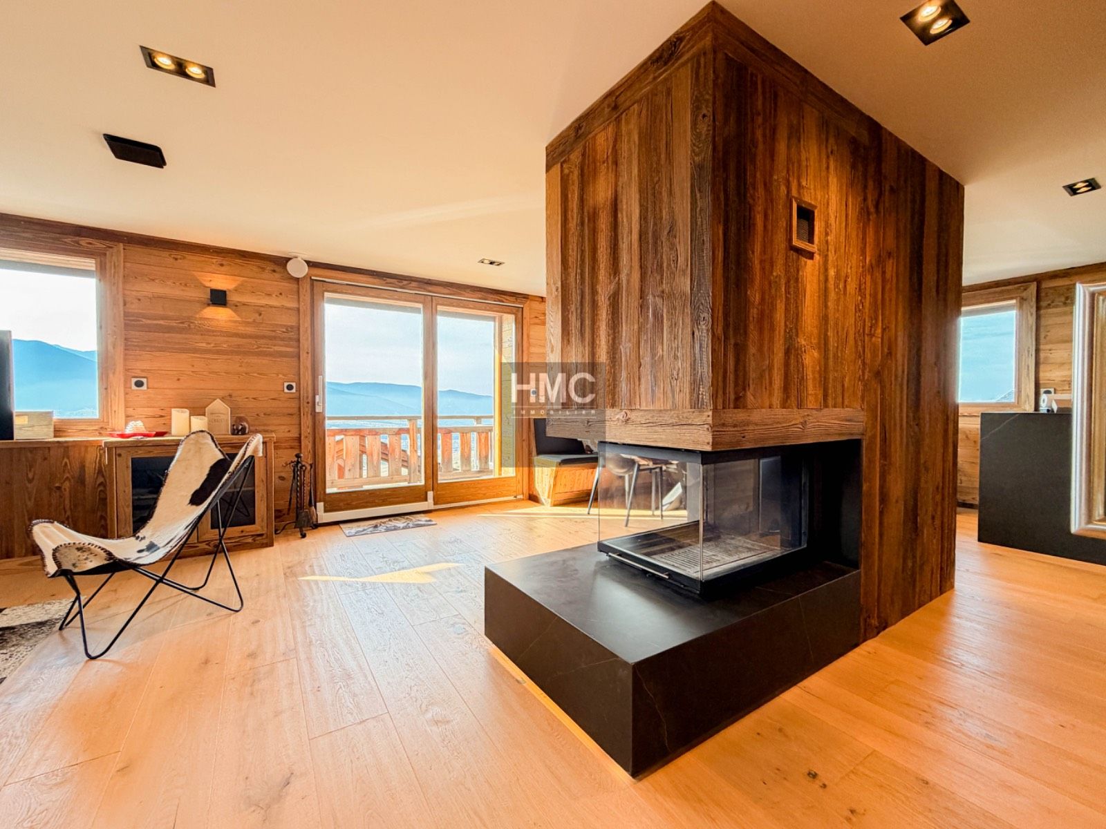 Ein modernes Interieur mit einer Wand aus Holz, einem Kamin und Blick durch große Schiebetüren.