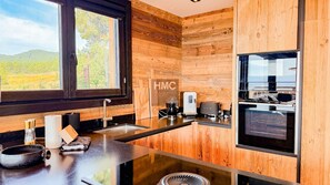 A modern kitchen with a wooden wall, a sink, a stove, and a window with a view of greenery. - Chalet Sélène — Jacuzzi, cheminée & vue sur les mo (Bolquère)