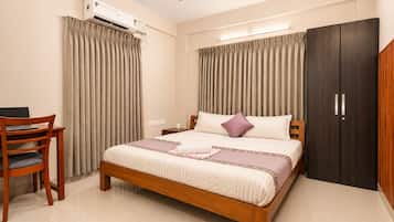 A bedroom with a bed, a desk, an air conditioning unit, a wardrobe, and a ceiling fan.
