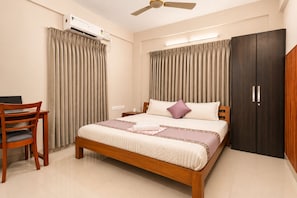 A bedroom with a bed, a desk, an air conditioning unit, a wardrobe, and a ceiling fan.