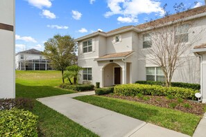 A two-story residential building with a front entrance, a covered patio, and a well-maintained lawn. - 5BR Townhouse Near Disney Pool & Oasis Club (Davenport)