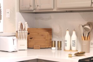 A kitchen counter with a toaster, a knife block, a wooden cutting board, and bottles labeled with cooking oils. - Cozy Modern 3br/2ba Retreat Near 3 Highways (Houston)
