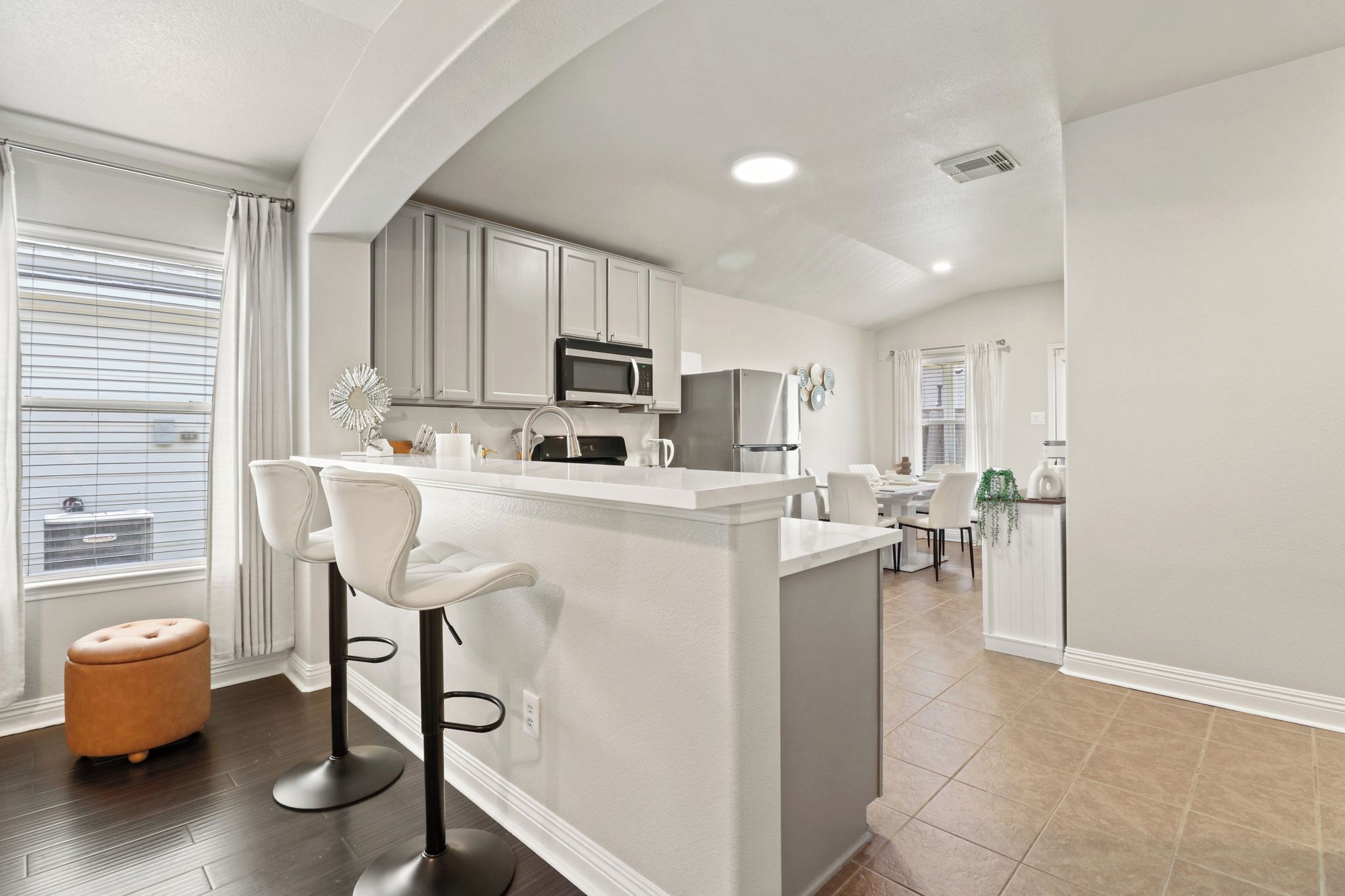 A modern kitchen with a central island, bar stools, and a dining area with a table and chairs.