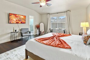 Ein Hotelzimmer mit Bett, Schreibtisch, Stuhl, Fernseher, einem Fenster mit Vorhängen und einem Deckenventilator.