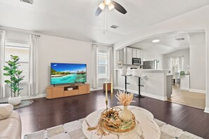 Ein modernes Wohnzimmer mit Flachbildfernseher, Deckenventilator und Essbereich mit Barhocker.