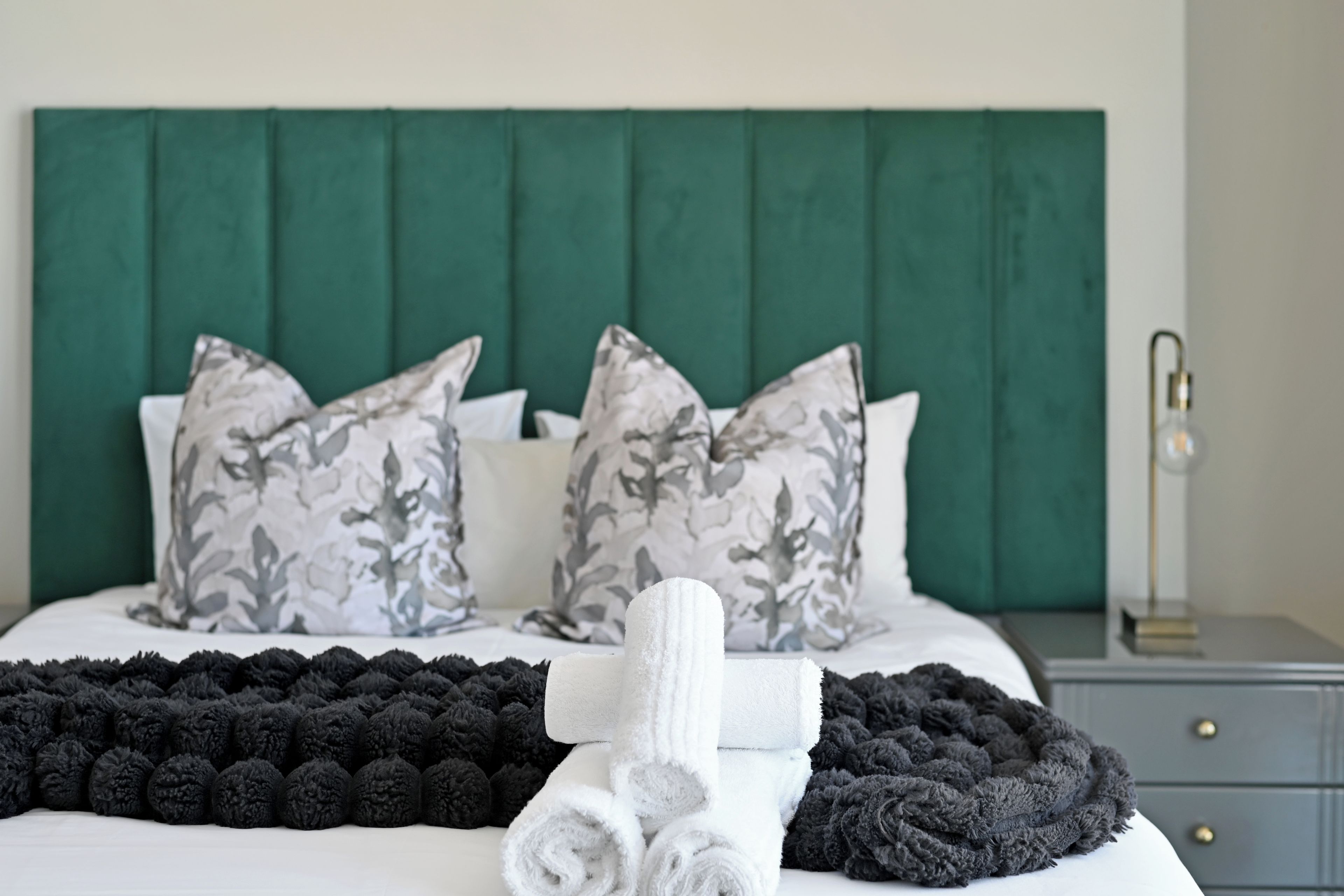 A neatly made bed with a green headboard, grey and white patterned pillows, and a black and white throw blanket.