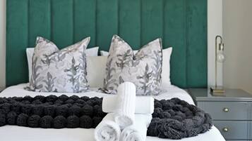 A neatly made bed with a green headboard, grey and white patterned pillows, and a black and white throw blanket.