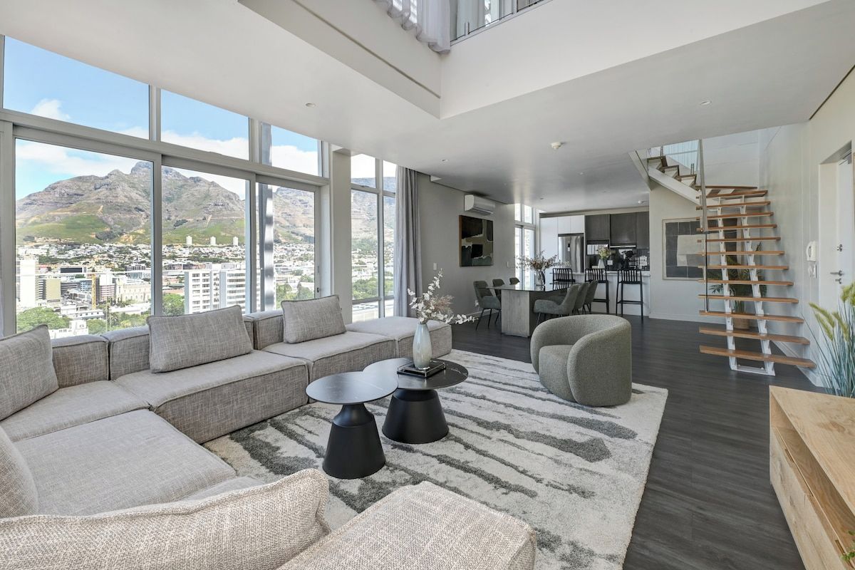 A modern living room with a large window, a sofa, a coffee table, and a staircase.