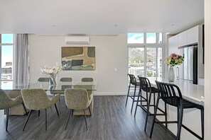 A modern dining area with a glass table, four chairs, and a vase of flowers. - Designer PH with 180° views of City, Mountain & Ocean in Cape Town (Cape Town)