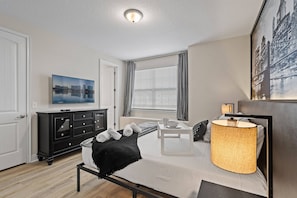 A modern bedroom with a bed, bedside table, lamp, and a cityscape painting. - 6BR Near Disney Private Pool & Game Room (Kissimmee)