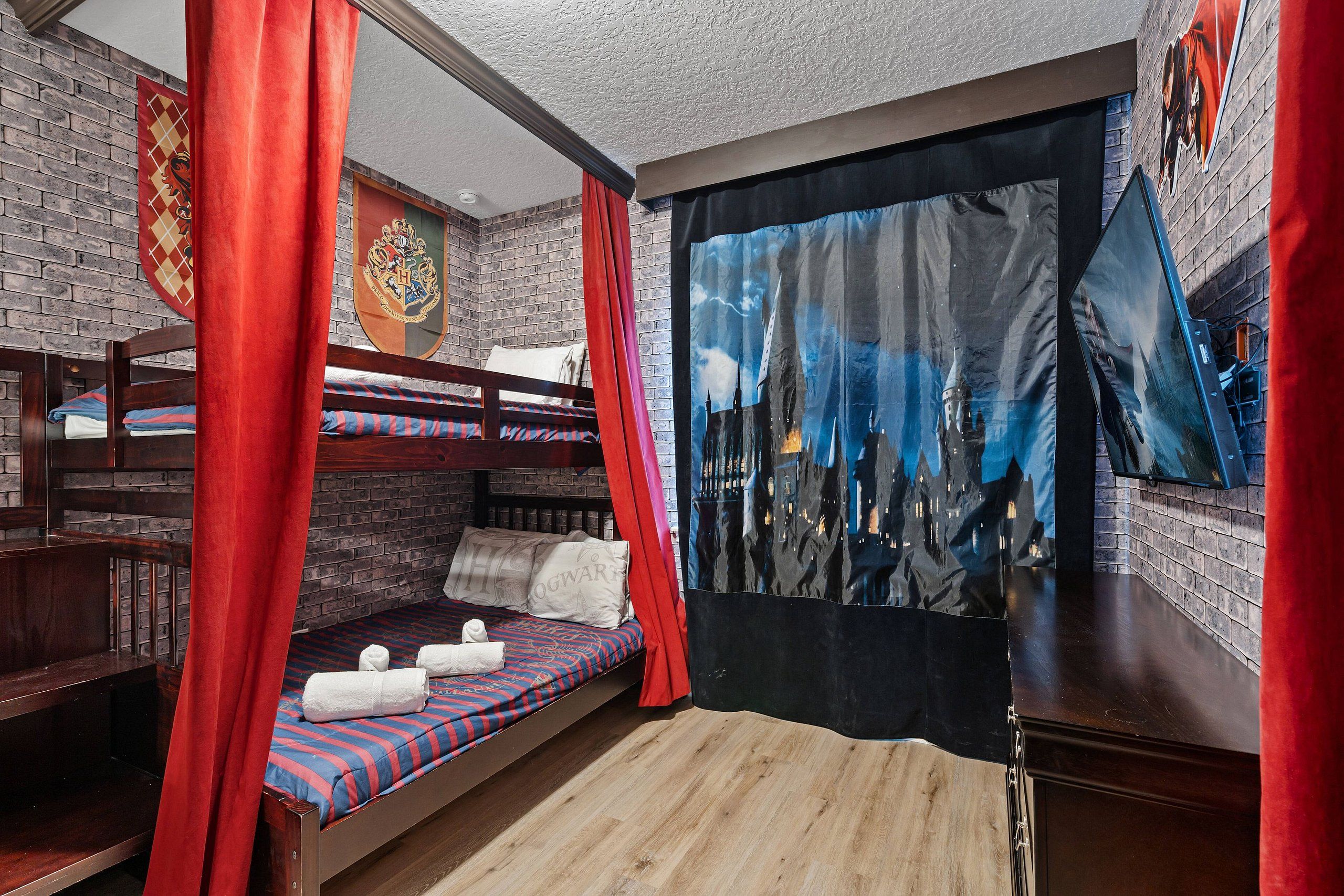 A room with a bunk bed, a flat bed with a castle-themed tapestry, and a red curtain.