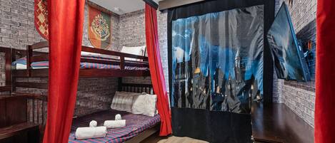 A room with a bunk bed, a flat bed with a castle-themed tapestry, and a red curtain.