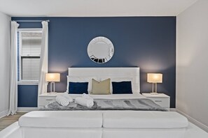 A bedroom with a large bed, two bedside tables with lamps, a wall-mounted mirror, and a window with blinds. - 6BR Near Disney Private Pool & Game Room (Kissimmee)