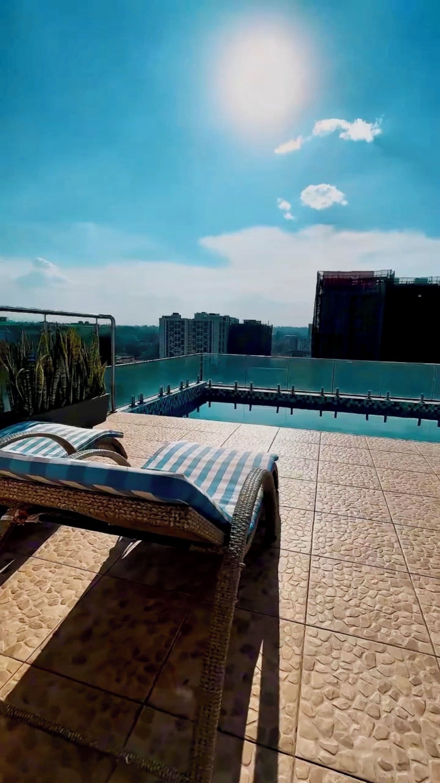 A sunlit outdoor area with a pool, lounge chairs, and a view of distant buildings.