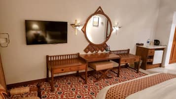 A hotel room with a wooden desk, a large mirror, a television, and a patterned floor.