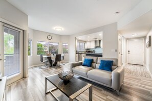 A modern living room with a sofa, coffee table, and dining area. - 2BR | En-Suite Bath • Pool • Spa • Free Parking (Las Vegas)