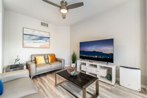 A modern living room with a sofa, coffee table, TV, and a white mini-fridge. - 2BR | En-Suite Bath • Pool • Spa • Free Parking (Las Vegas)