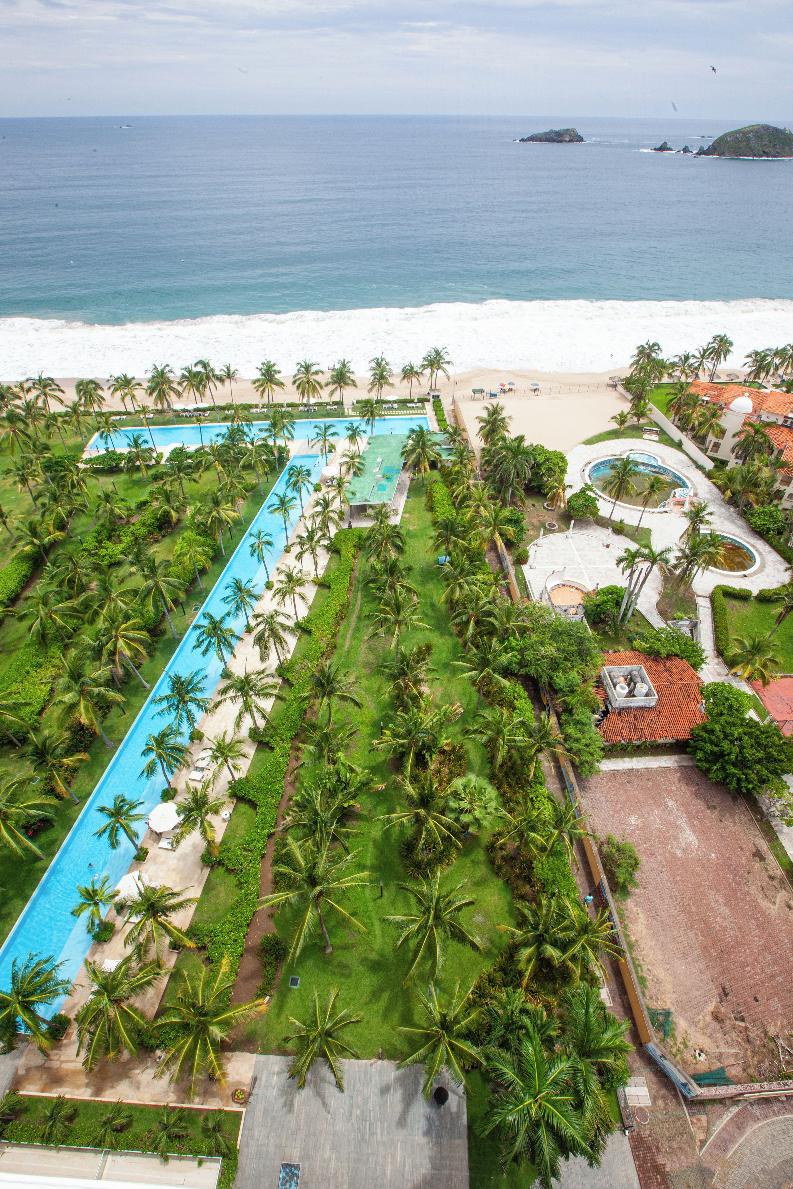 A resort with a long swimming pool, palm trees, and a beach view.