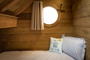 A wooden cabin room with a round window, a bed with white bedding, and a pillow with a star pattern. - Newly Built Chalet - Charm and Authenticity - Liza's Dacha (Muhlbach-sur-Munster)